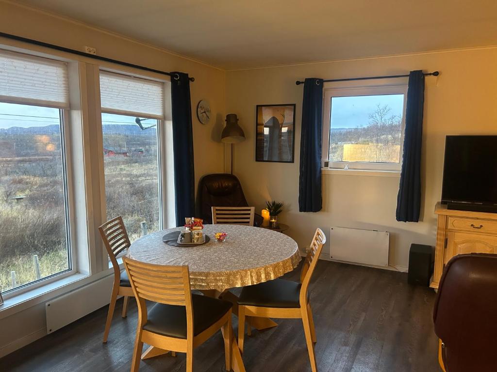 a dining room with a table and chairs and two windows at Suovka reindeer & bird lodge in Varangerbotn