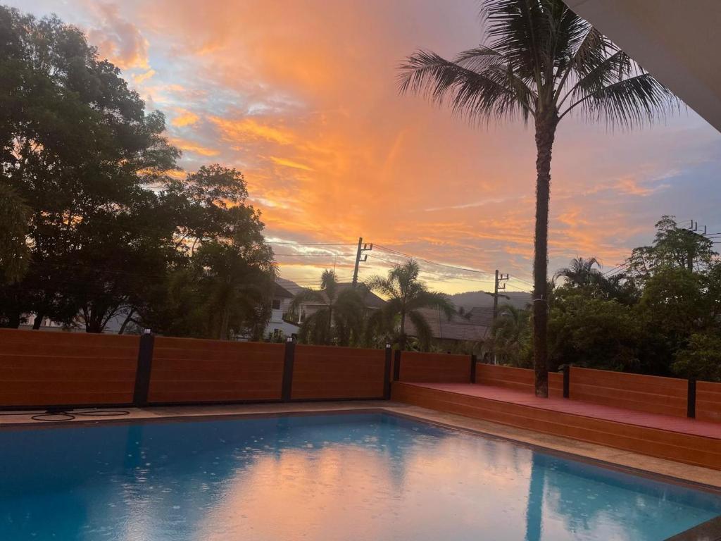 a swimming pool with a palm tree and a sunset at Khao Lak - Loft Suite with 2 king size beds, bathroom with bathtub in Khao Lak