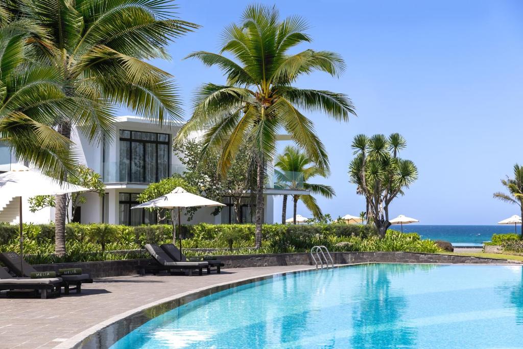 A curved resort pool beside palms and loungers with the sea beyond.