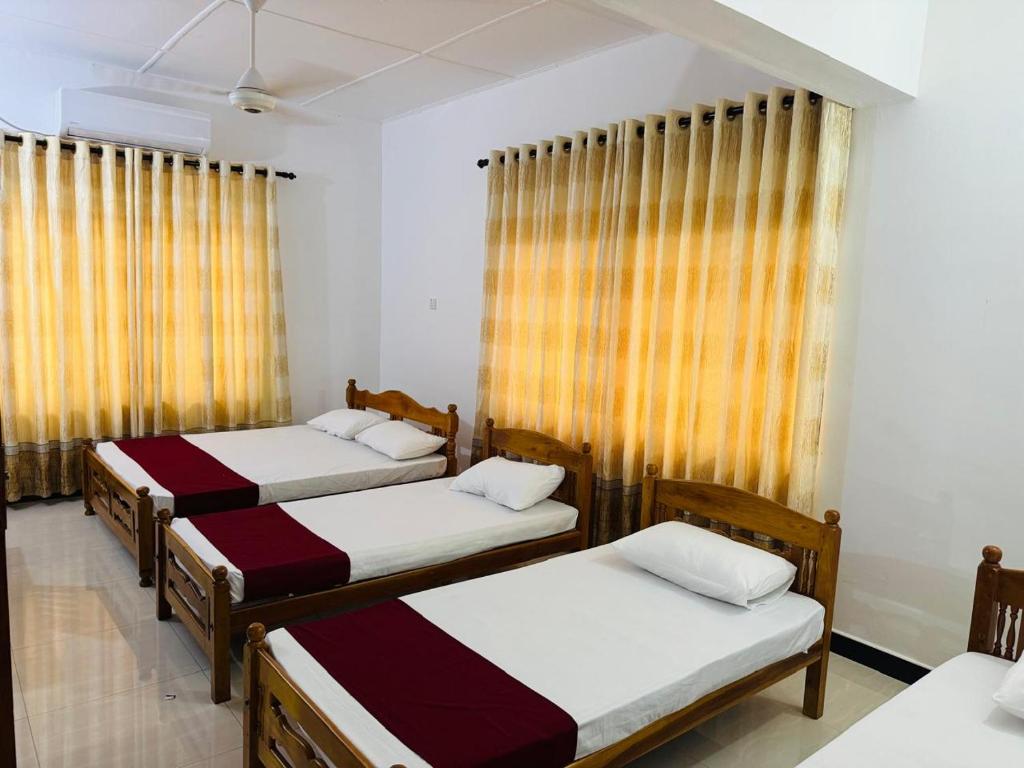 drie bedden in een kamer met gele gordijnen bij Vinola Hotel in Mannar