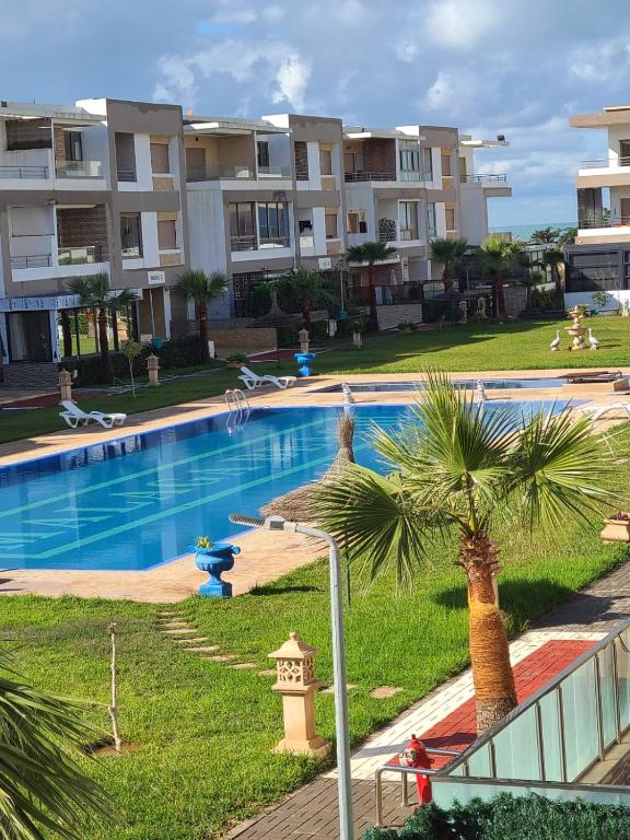 a swimming pool with a palm tree and some buildings at santa barbara in Mansouria