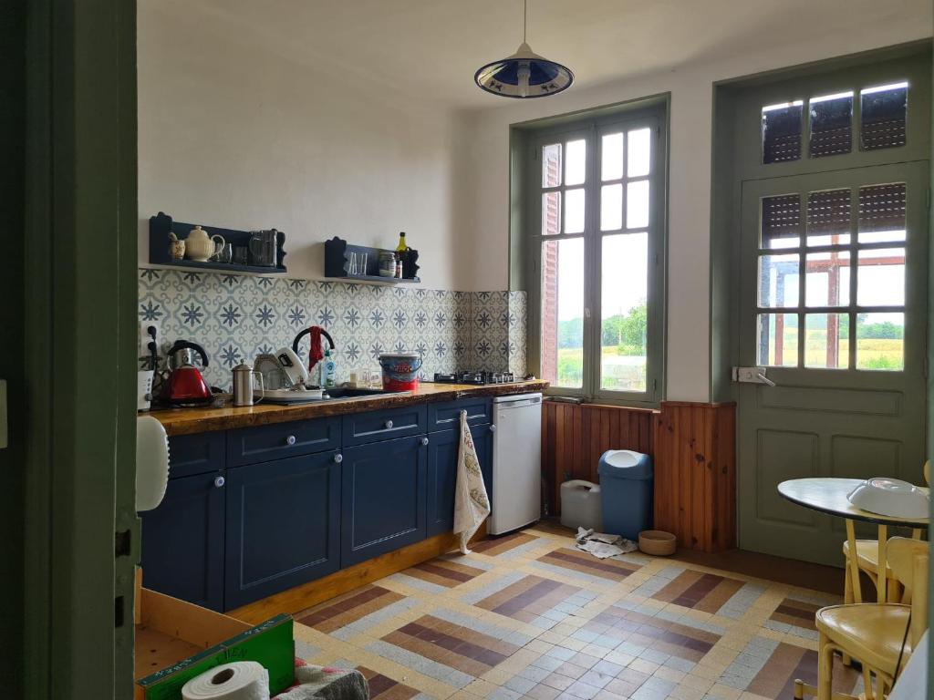 une cuisine avec des armoires bleues, une table et une fenêtre dans l'établissement Maison Huitlala, à Lavaufranche