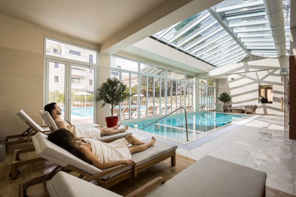 deux personnes assises sur des chaises dans un salon avec piscine dans l'établissement Hôtel Miléade L'Orangeraie - entièrement rénové, à Menton