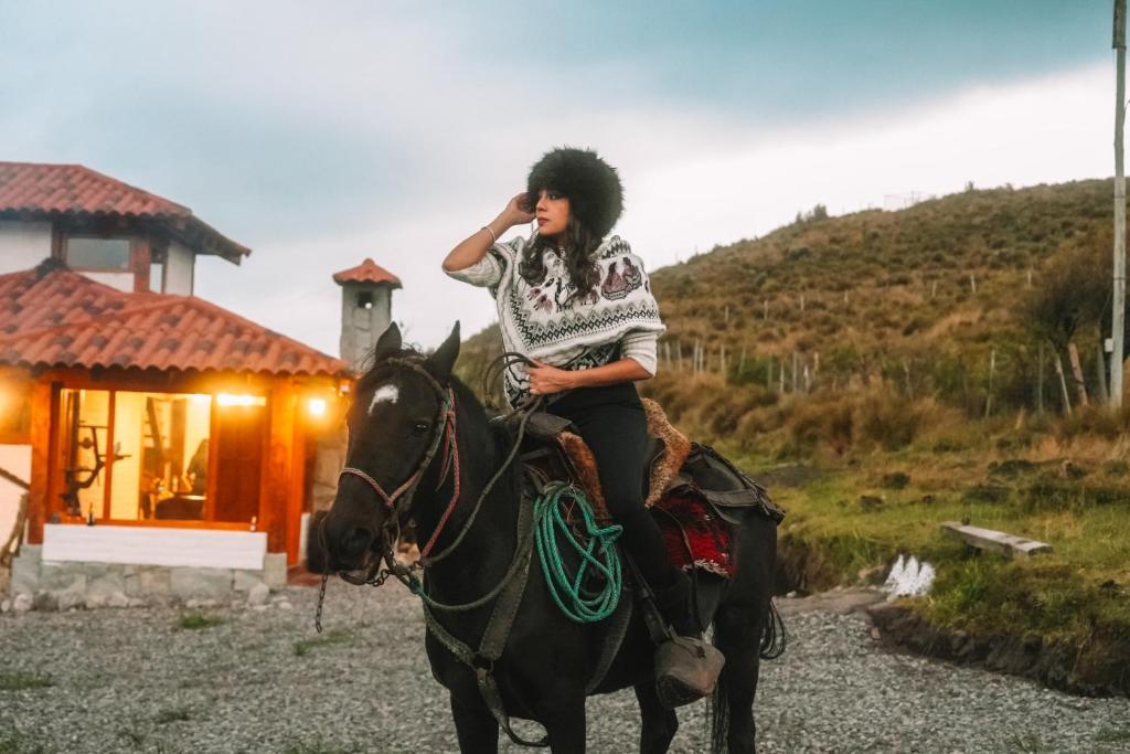 Una donna che cavalca un cavallo davanti a una casa di Solarium Cabaña a Riobamba