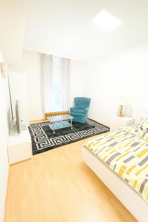 a white bedroom with a bed and a blue chair at Beenie 19 in Linz