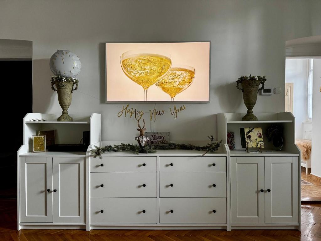 Twee witte dressoirs in een kamer met een schilderij aan de muur. bij Forst Apartman in Eger