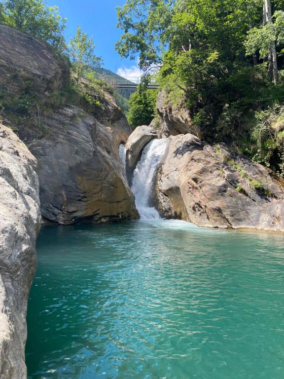 a waterfall next to a river with green water at Waterfall House - Art and Design, Ski, Hike, Swim in Mesocco