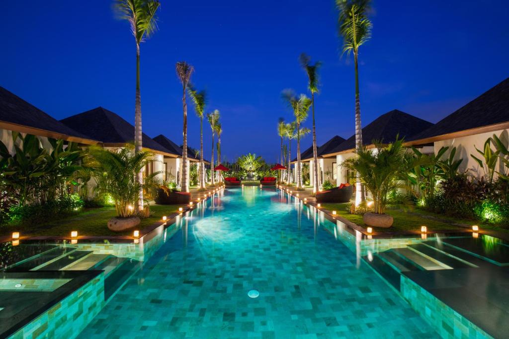 a swimming pool at night with palm trees and lights at Villa Naty in Canggu