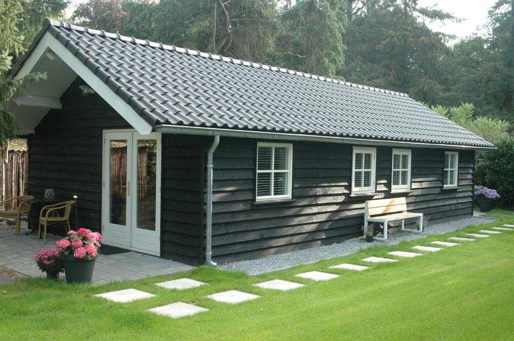 a small black cabin with a bench in the yard at Aan de Bosrand Hoenderloo in Hoenderloo