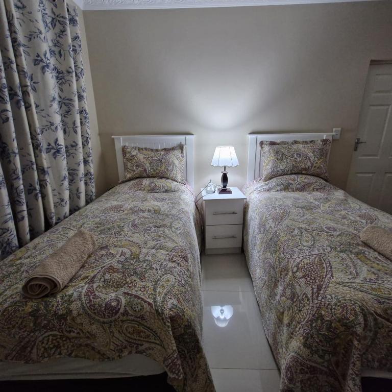 two twin beds in a bedroom with a lamp on a night stand at Ashley's Cottage in Himeville