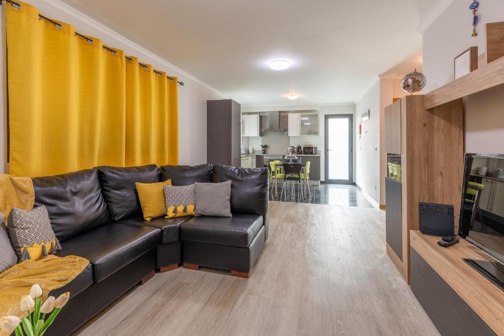 ein Wohnzimmer mit schwarzem Ledersofa und gelben Vorhängen in der Unterkunft Apartamento Ruby in Machico