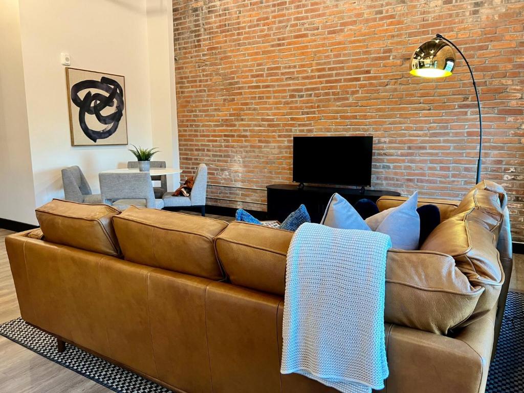 a brown couch in a living room with a brick wall at Brick & Bed Riverfront Lofts, T 302 in Saint Louis