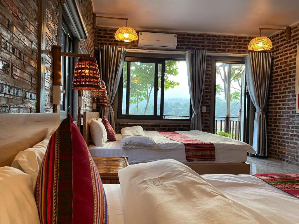 1 Schlafzimmer mit 3 Betten und Ziegelwand in der Unterkunft Nha Tan - Mai Chau Homestay & Tours in Mai Châu