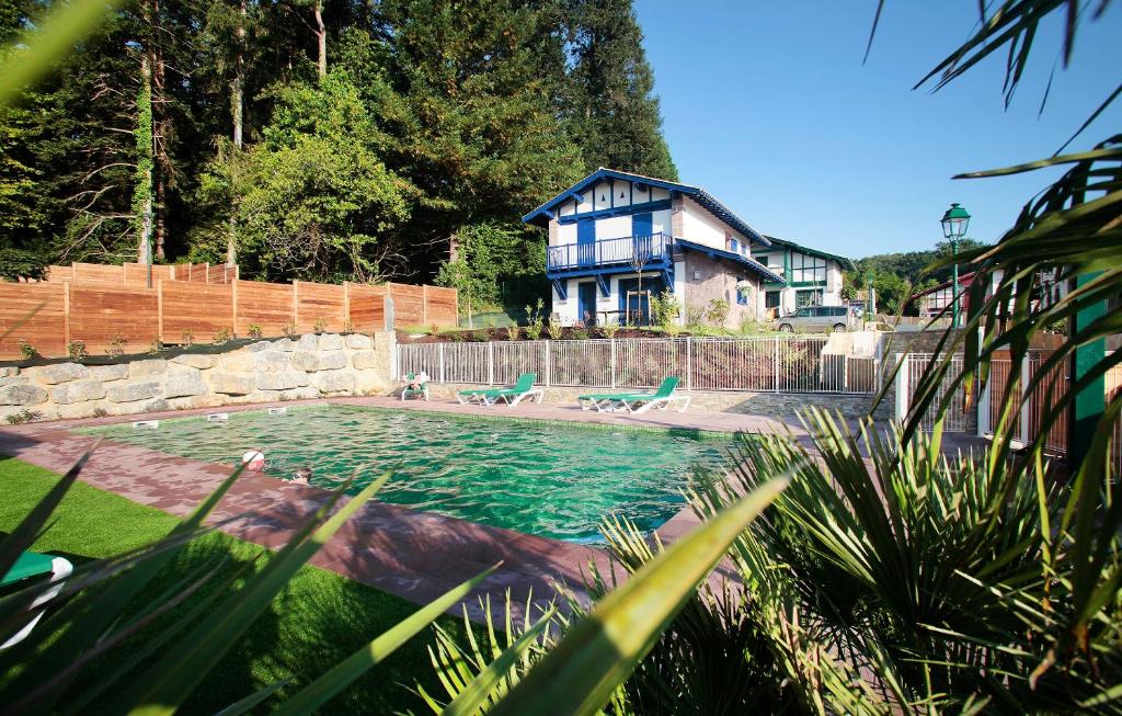 ein Schwimmbad mit einem Haus im Hintergrund in der Unterkunft Résidence Prestige Odalys Le Domaine de Lana in Urrugne