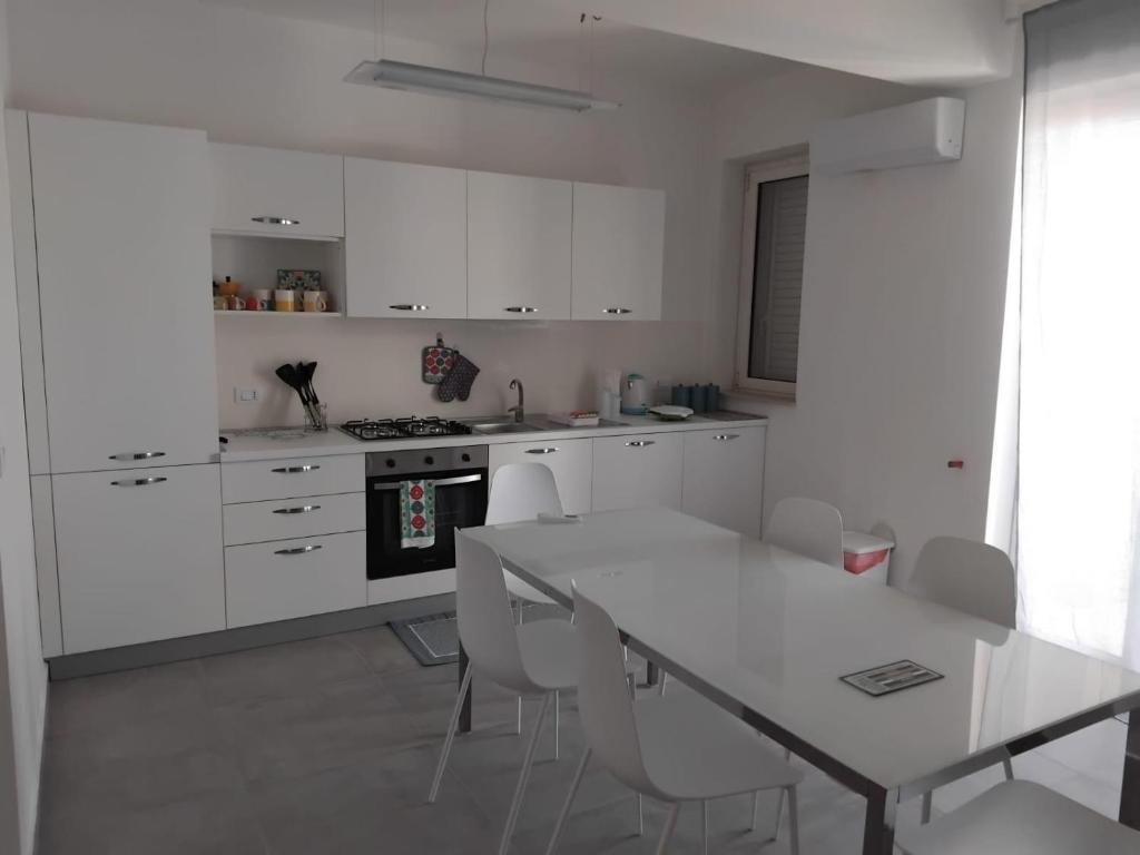 een keuken met witte kasten en een witte tafel en stoelen bij Marie Plus In Centro in Capo dʼOrlando
