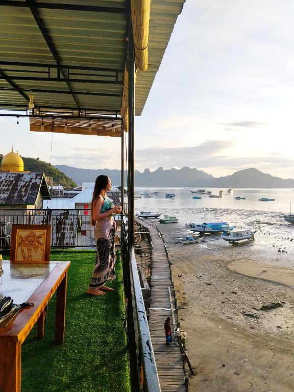 a woman standing on a balcony looking at the beach at Bajo Komodo Homestay in Komodo