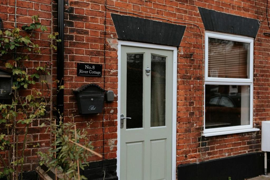 a brick building with a white door and windows at River Cottage in Beccles