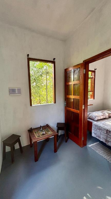 a room with a table and a bed and a window at Taboca Chalé na Rua do Serrão in Cairu