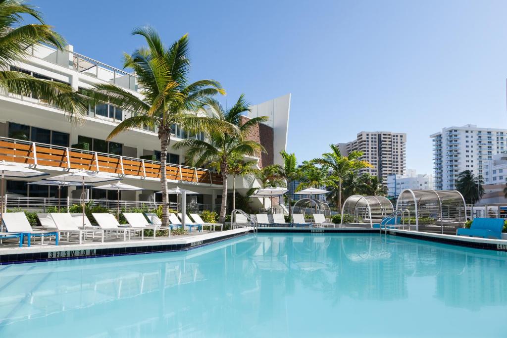 a large swimming pool with chairs and palm trees at The Gates Hotel South Beach - a Doubletree by Hilton in Miami Beach
