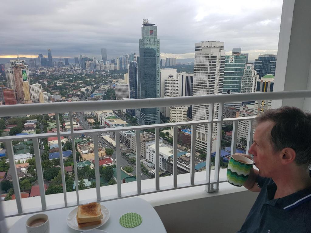 馬尼拉的住宿－All At Jazz - Makati Serviced Apartments，男人在市景阳台喝一杯