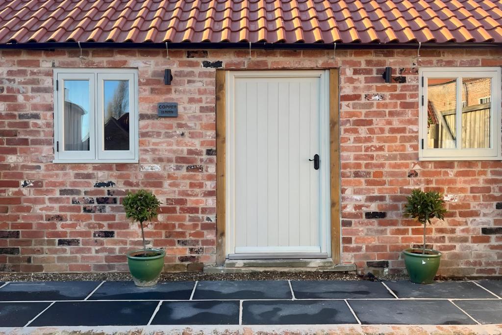 ein Backsteinhaus mit einer weißen Tür und zwei Topfpflanzen in der Unterkunft Coach Lodge in Torworth