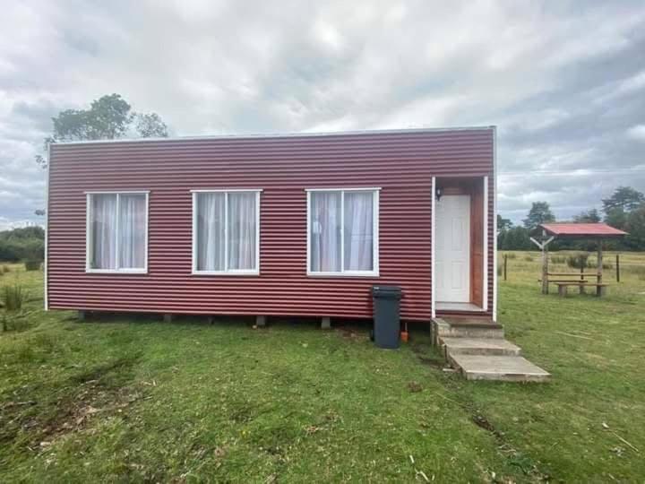 a small red house in a field with a table at Cabañas Mocopulli in Dalcahue