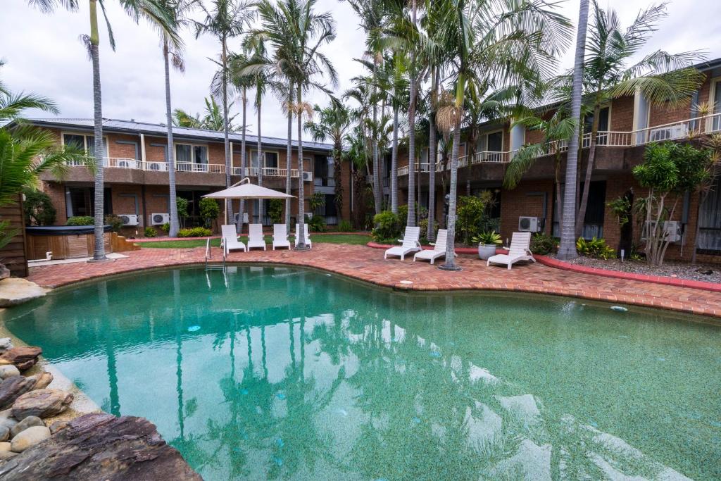 una piscina frente a un hotel con palmeras en The Galaxy Motel en Gosford