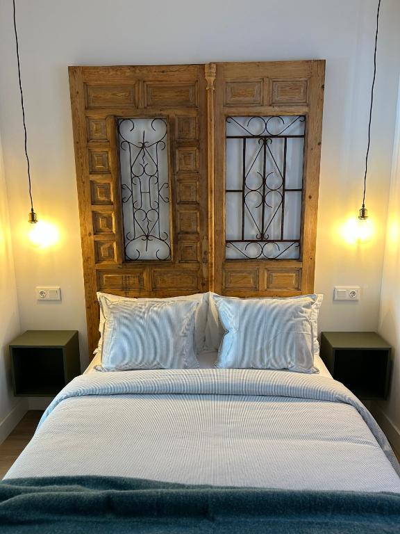 a bed with a wooden headboard and two windows at La Baltasara Apartments in Valladolid