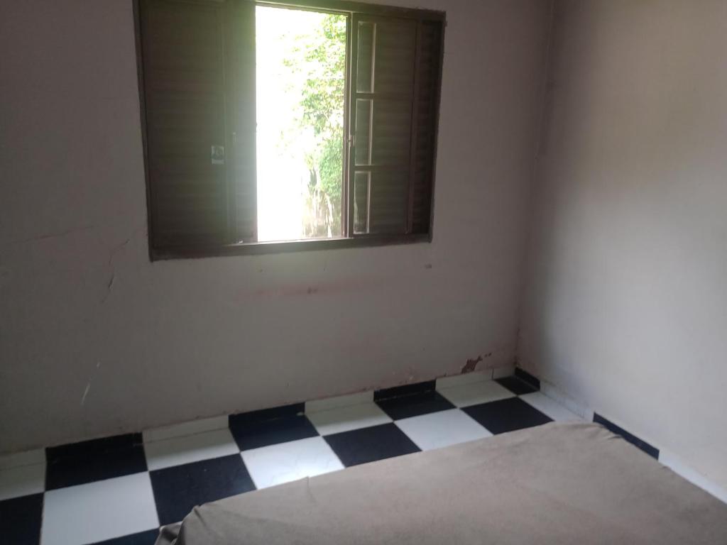 a room with a bed and a window and a checkered floor at QUARTO lado praça colchão sob estrado in Chapada dos Guimarães