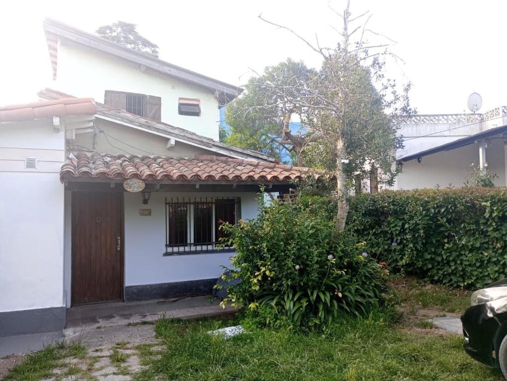 a white house with a brown door and a hedge at La Carioca in Villa Gesell