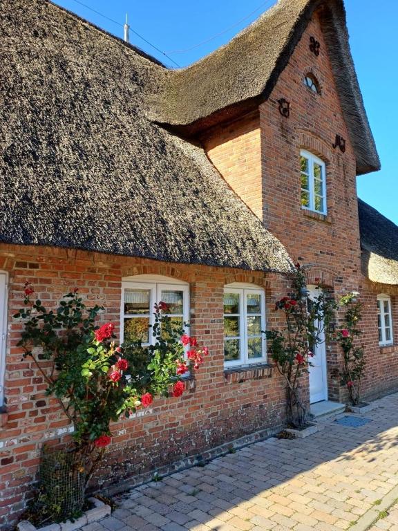 a brick house with a thatched roof with flowers at Lykke in Wrixum