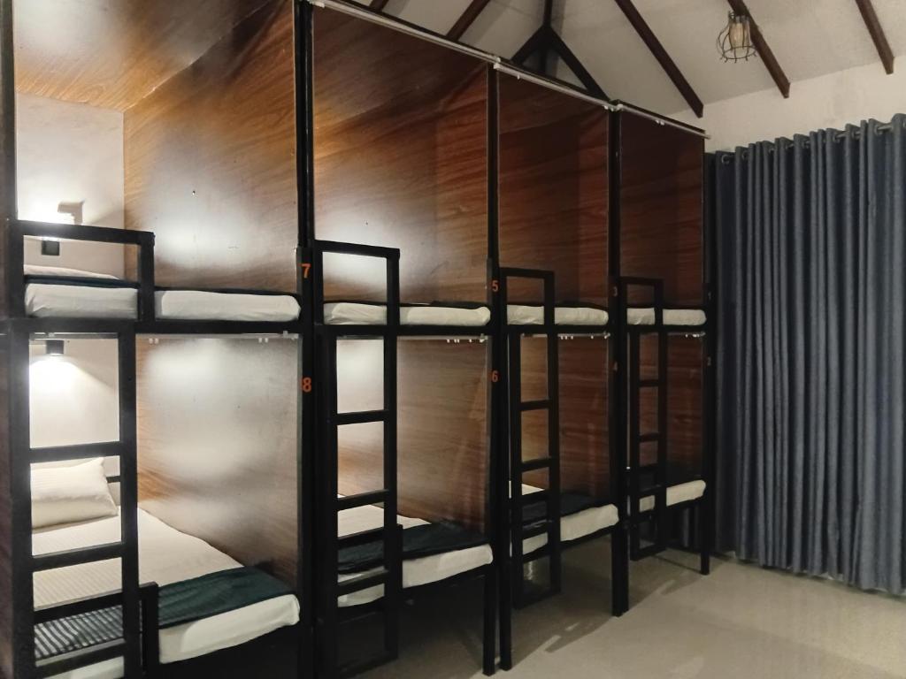 a room with three bunk beds and a wooden wall at One More Night Hostel in Sigiriya