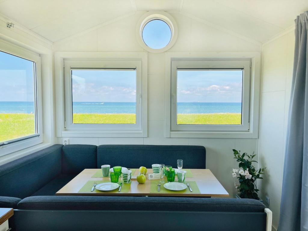 a living room with a table and three windows at Strandhaus James Cook Teichhof Fehmarn in Wenkendorf