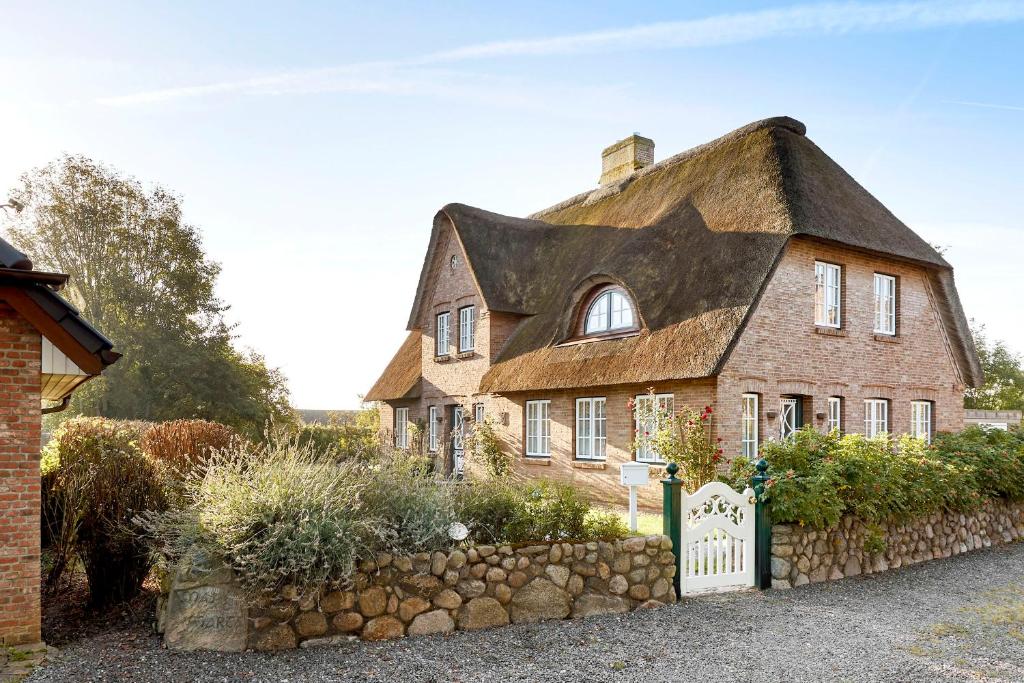 ein altes Haus mit Strohdach und Steinzaun in der Unterkunft Reethüs Maj - links in Utersum