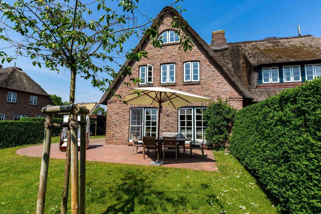 a house with a table and an umbrella in the yard at Reetdachhaus Hedehusum in Hedehusum