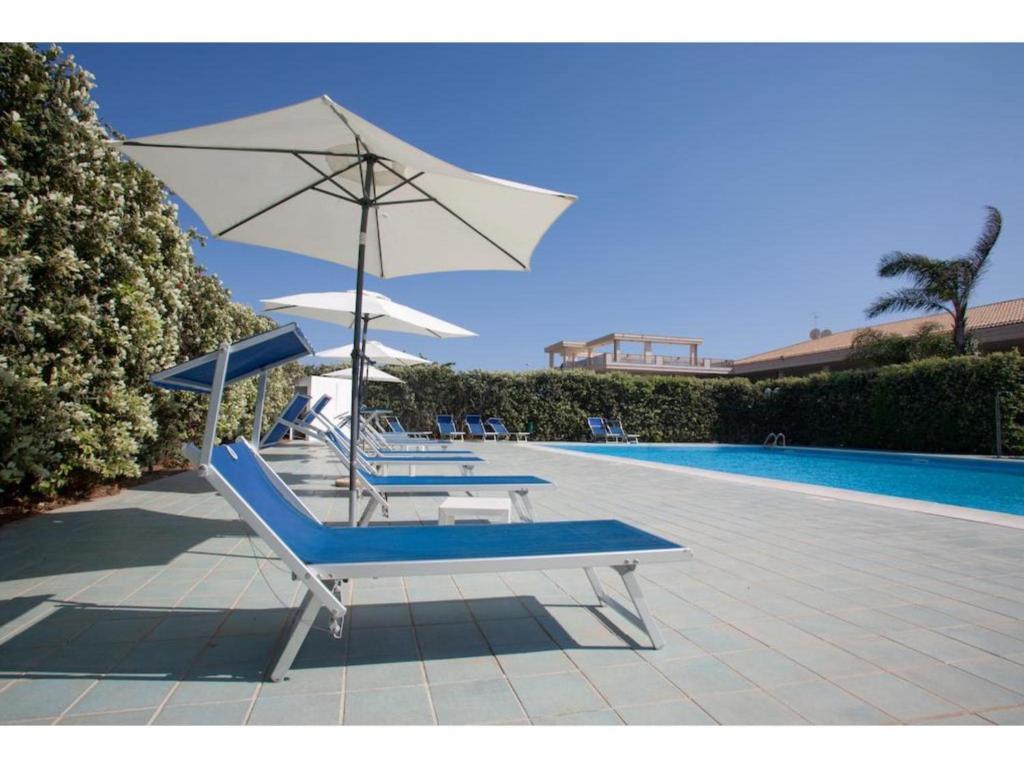 2 ligstoelen en een parasol naast een zwembad bij Pretty Apartment in Scoglitti, Sicily in Scoglitti