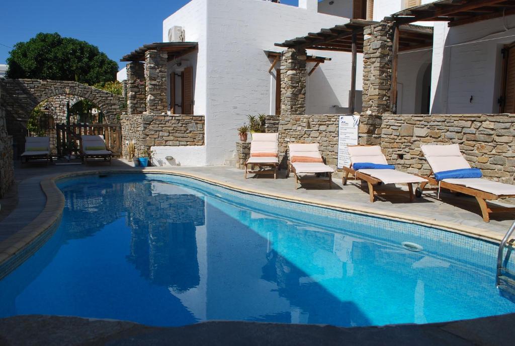 a swimming pool with chairs and a house at Siroco's Rooms And Studios in Parikia