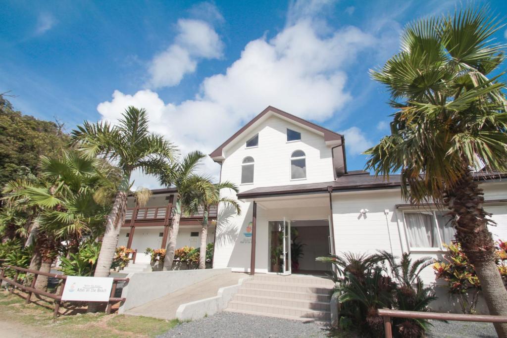 a white house with palm trees in front of it at Native Sea Amami Adan On The Beach in Tatsugo