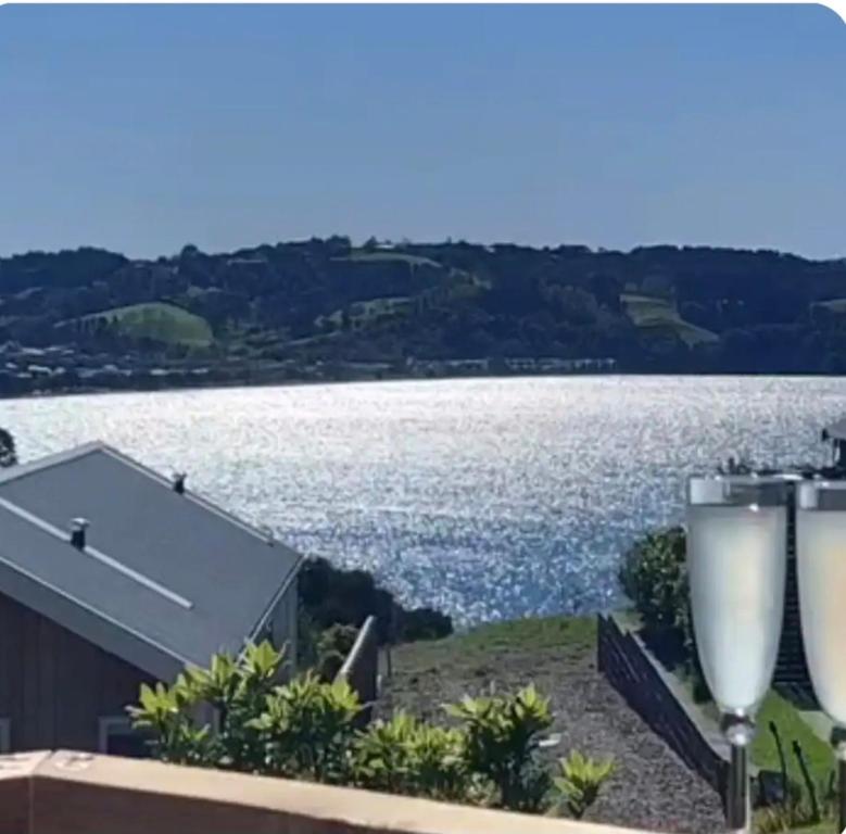 two wine glasses sitting on a balcony overlooking a lake at Tide and Tranquility in Snells Beach
