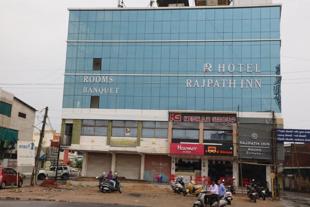 a tall building with people riding motorcycles in front of it at Hotel Rajpath Inn in Mahesāna