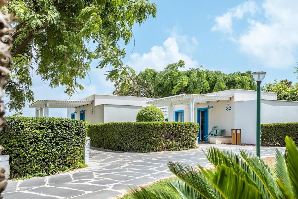 ein weißes Haus mit grünen Hecken davor in der Unterkunft Nachsholim Beach Hotel in Nachscholim