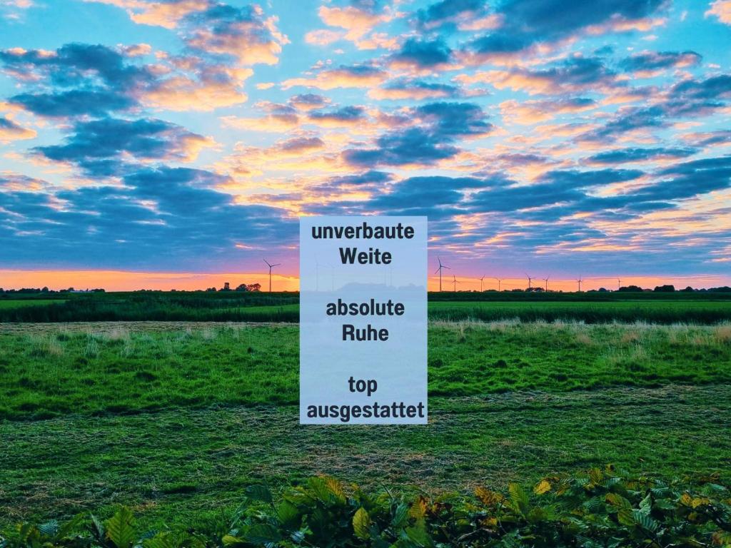 un cartello bianco in mezzo a un campo di Ferienhaus Robbenglück in Tossens - Ihr gemütliches Zuhause an der Nordsee a Tossens