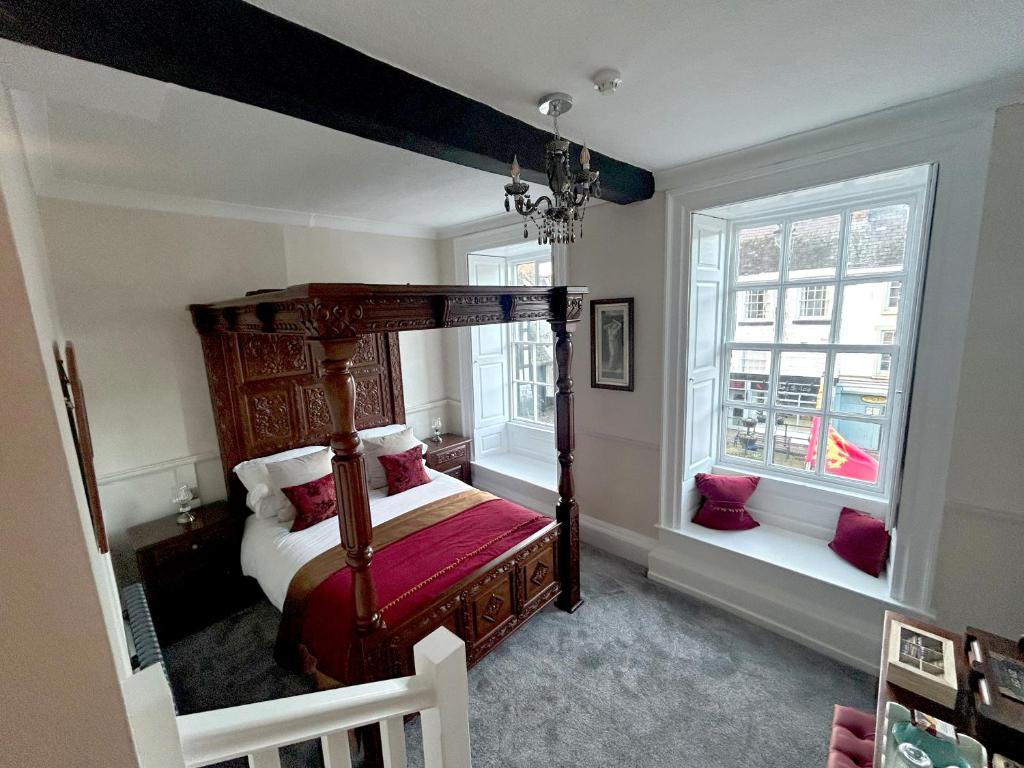 a bedroom with a canopy bed and two windows at Community Owned Gwesty Owain Glyndwr Hotel in Corwen