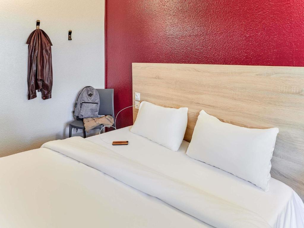 a bedroom with a white bed with a red wall at hotelF1 Chaumont in Chaumont