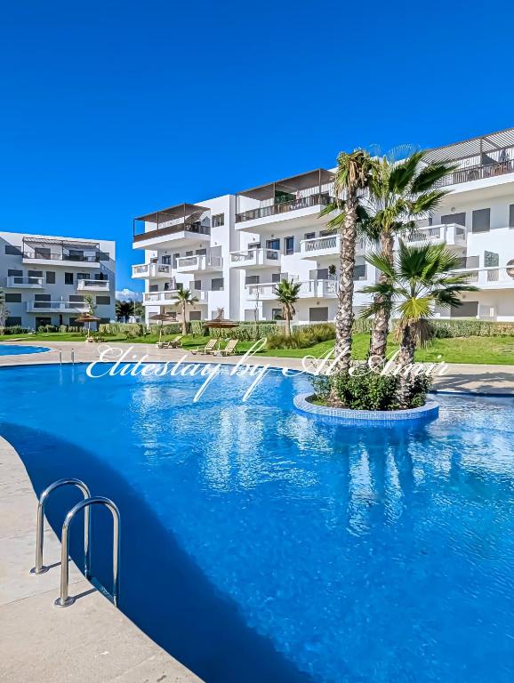 a large swimming pool with palm trees in front of a building at Elite'Stay by Al Amir in Cabo Negro
