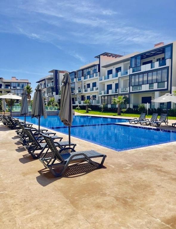 a row of lounge chairs and umbrellas next to a swimming pool at Appartement tamaris les crêtes in Casablanca