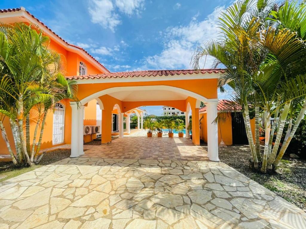 an orange house with a stone walkway and palm trees at Villa Tropical Cabarete in Sosua