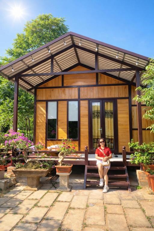 a woman sitting on a bench in front of a house at Thu May Homestay A Lưới in A Lưới (1)