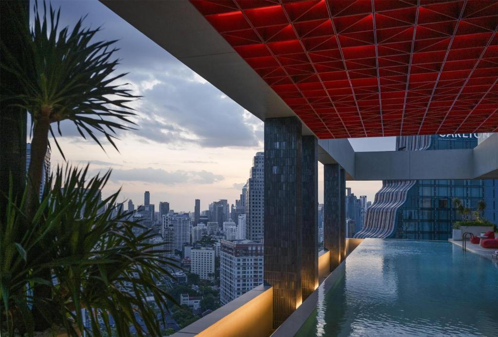 An elevated pool terrace with a dramatic dusk skyline and a red geometric canopy.