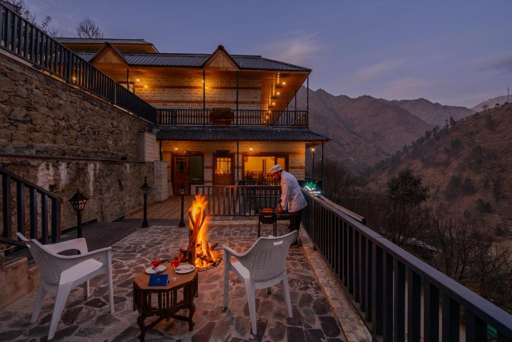 a man standing on the balcony of a house with a fire at SaffronStays Tirthan House - Balcony View in Bandal